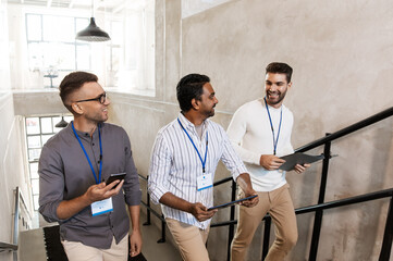 business, people and corporate concept - men with conference badges, folder, tablet pc computer and smartphone walking up office stairs