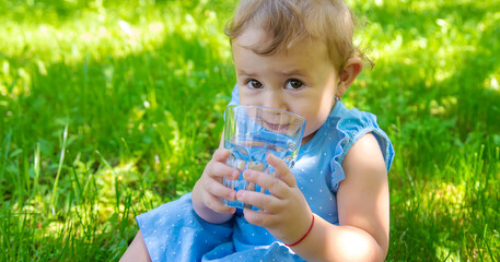 The child drinks water from a glass. Selective focus.