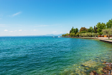 Lakefront of the small Bardolino village with the pedestrian and bicycle lane. Tourist resort on the coast of Lake Garda. Verona province, Veneto, Italy, southern Europe. On horizon the Lombardy coast