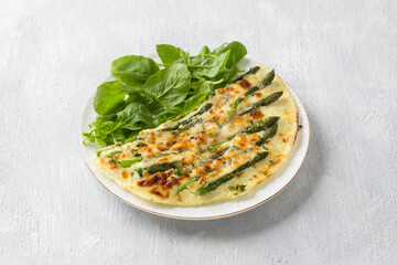 Delicious omelette with asparagus and cheese on a white plate on a light gray background, top view....