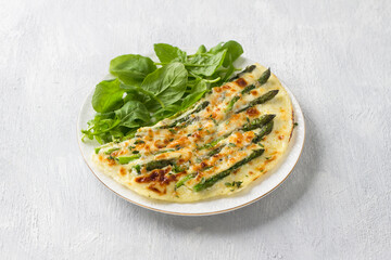 Delicious omelette with asparagus and cheese on a white plate on a light gray background, top view. Homemade vegetarian food