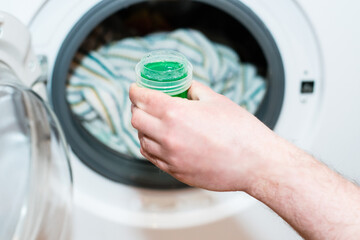 Washing gel close up in male hand on the background of the washing machine with linen