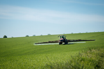 Tractor spraying insecticide at field. Agricultural activity at springtime. Cultivated land in...