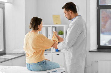 Obraz premium medicine, healthcare and people concept - male doctor with clipboard talking to woman showing her sore arm patient at hospital