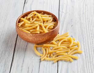 Uncooked maccheroni pasta in wooden bowl on white wooden background