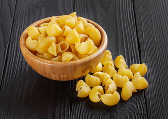 Uncooked pipe rigate pasta in wooden bowl on black wooden background