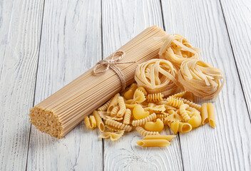 Different types and shapes of Italian pasta on white wooden background