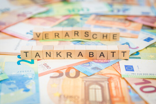 Das Wort Tankrabatt &ndash; in deutsch f&uuml;r Fuel discount -  und verarsche  &ndash; in deutsch f&uuml;r fooling -  im Hintergrund auf Geldscheine Euro Euroscheine mit Holzw&uuml;rfel geschriebener Text