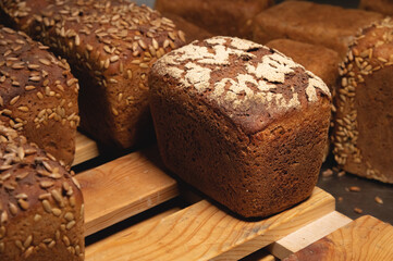 Close-up rye loaves of hot rye bread stand on a wooden tray in a dark bakery room