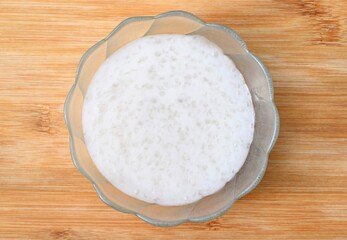 Homemade tapioca pudding with coconut milk in a glass bowl, wooden background