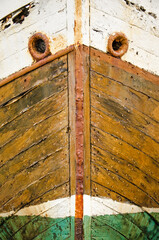 Front view of the bow of an old wooden boat, with rusty steel details, painted in bright but fading colors