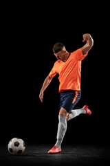 Studio shot of professional male football soccer player in motion isolated on dark background....