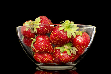 Several berries of ripe organic strawberries in a glass dish, close-up, isolated on a black background.