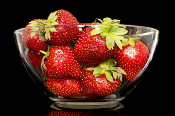 Several berries of ripe organic strawberries in a glass dish, close-up, isolated on a black background.
