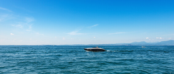 Speedboat in motion on Lake Garda (Lago di Garda) in front of the small Bardolino village, tourist resort in Verona province, Veneto, Italy, Europe. On horizon the coast of Lombardy.