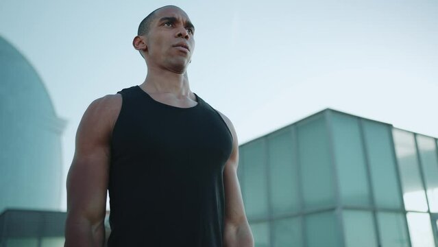 Bald concentrated sportsman wearing black T-shirt doing sport exercises with an elastic band outdoors in the morning