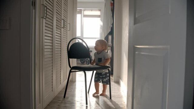 A little baby boy drags a chair among the corridor