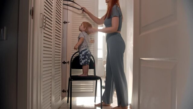 A little baby stands on the chair and throws away a