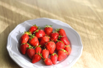 Lilac plate full of fresh strawberries on wooden table. Selective focus.