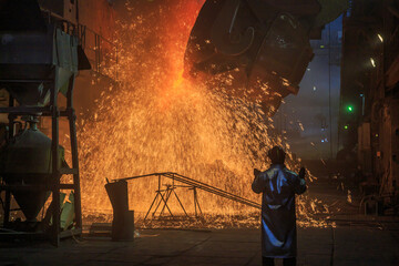 Hot steel pouring from big casting ladle into a mold in an iron foundry.