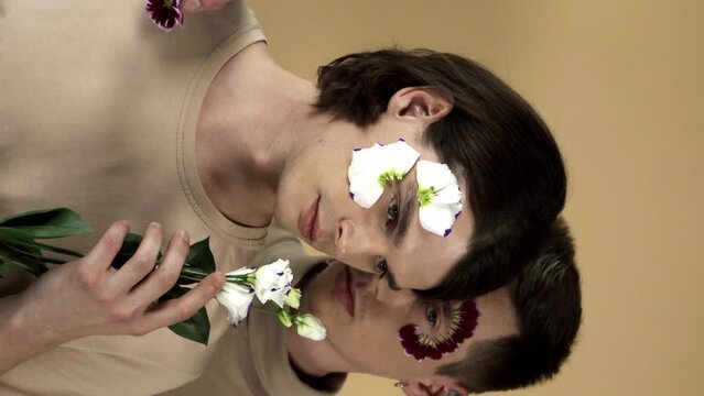 young gay couple with white eustoma flower and petals on faces isolated on beige