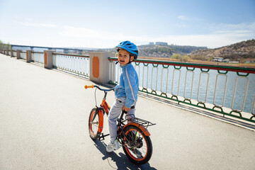 a happy smiling boy on a bicycle in a blue jacket and helmet 