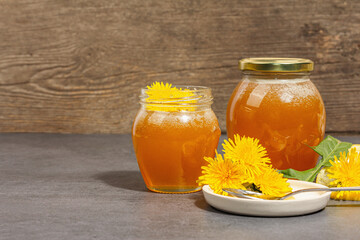 Dandelion jam or honey in the glass jar with fresh dandelion flowers. Trendy hard light, dark shadow