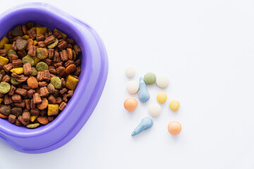 top view of plastic bowl with dry pet food near vitamins in pills isolated on white.