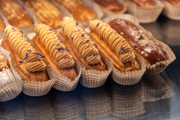 Eclairs on the shelf of a pastry shop or cafe. Tasty french sweets on window shop, delicious pastries for coffee. Cakes in pastry shop, variety of desserts with creamy topping on display in bakery