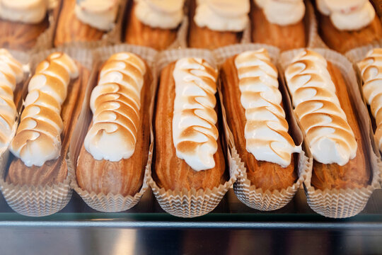 Eclairs on the shelf of a pastry shop or cafe. Tasty french sweets on window shop, delicious pastries for coffee. Cakes in pastry shop, variety of desserts with creamy topping on display in bakery