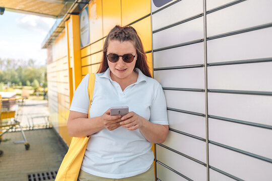 Woman picks up mail from automated self-service post terminal machine. Parcel shipping service or delivery packaging concept