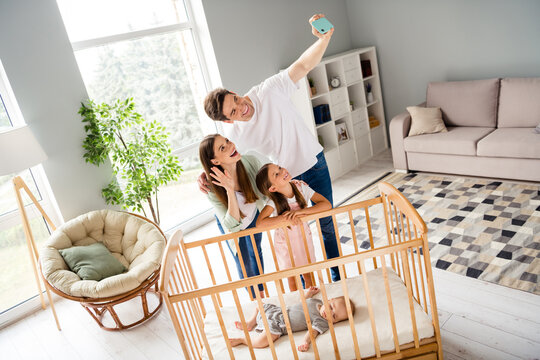 Photo of positive excited family make selfie hand wave hello greetings toddler sleep crib home indoors