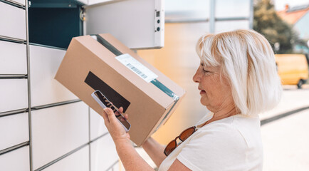 Caucasian 50s 60s woman picks up mail from automated self-service post terminal machine. Mail shipping concept