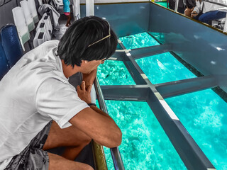 Male tourist looks at coral reefs through the transparent bottom of a ship in Sharm El Sheikh,...