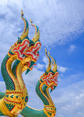 Fototapeta na wymiar Low angle and side view of 2 colorful 3-headed serpent statues against white clouds on blue sky background in vertical frame