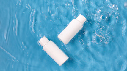 White cosmetic bottles in a blue pool. Moisturizing lotion for skin and body and spa treatments. Template for design.