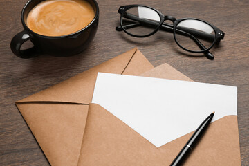 Envelopes with blank paper card, cup of coffee, glasses and pen on wooden table, closeup