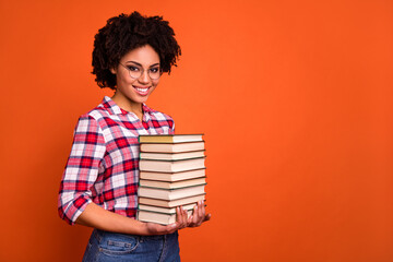 Photo of cheerful pretty person arms hold stack book empty space ad isolated on orange color background