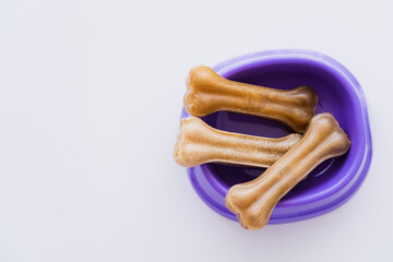 top view of bone shaped pet treats in purple bowl isolated on white.