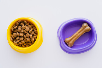 top view of bone shaped pet treats in bowl near dry pet food isolated on white.