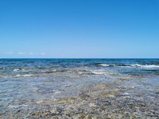 The coast of the Mediterranean Sea, waves, clear water, through which you can see the stone bottom. All this against a blue sky with clouds.