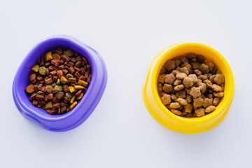 top view of plastic bowls with different pet food isolated on white.