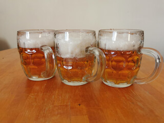 Three small glass mugs with light beer with foam, standing on a wooden table, on a light background.