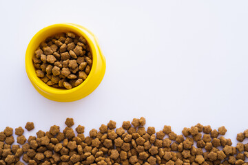top view of yellow plastic bowl with dry pet food isolated on white.