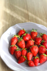 Lilac plate full of fresh strawberries on wooden table. Selective focus.