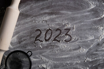 2023 numbers on scattered flour on a table next to a rolling pin for dough