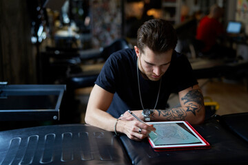 Caucasian tattoo artist  designing motifs on digital tablet