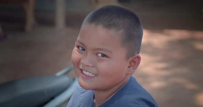 Slow motion scene of a happy smiling Asian farmer boy wearing traditional clothes who is the son of an Asian farmer family, sitting on a bamboo cowshed.