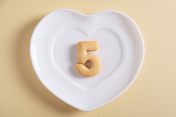 Biscuits forming number 5 on the white plate and yellow light background