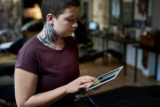 Caucasian tattoo artist sitting at the studio and looking on digital tablet